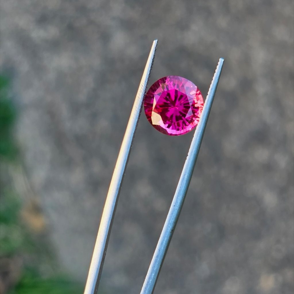 Electric cherry Burmese spinel in tweezers in natural daylight