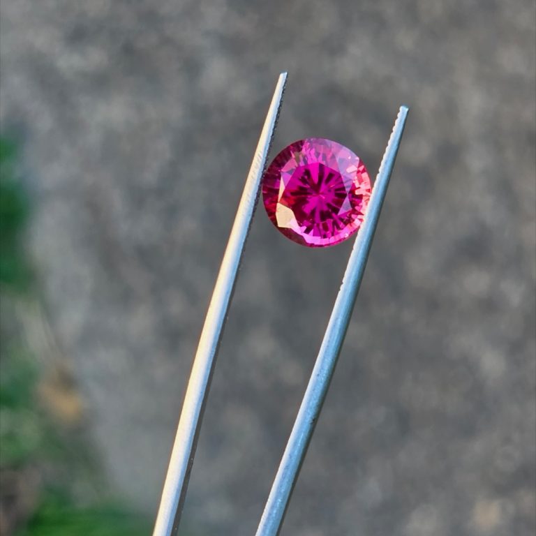 Electric cherry Burmese spinel in tweezers in natural daylight