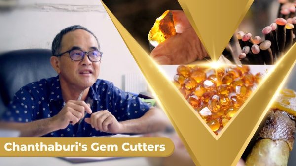 The owner of a Chanthaburi gem cutting factory beside a pile of cut yellow and orange gemstones, from the video Chanthaburi's Legendary Gem Cutters