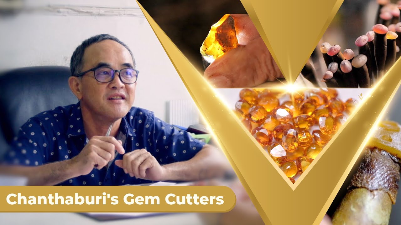 The owner of a Chanthaburi gem cutting factory beside a pile of cut yellow and orange gemstones, from the video Chanthaburi's Legendary Gem Cutters