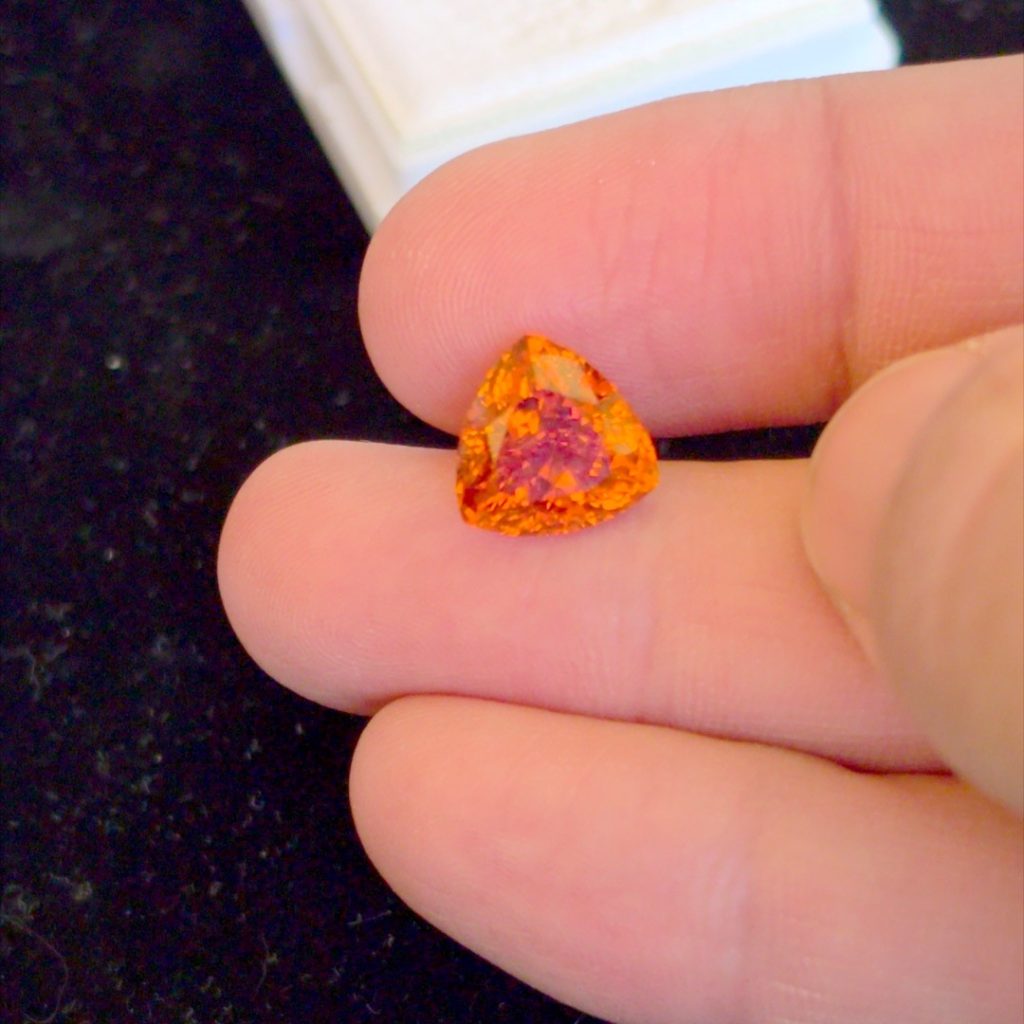 7 carat Fanta orange spessartine garnet in a trillion cut, held between fingers