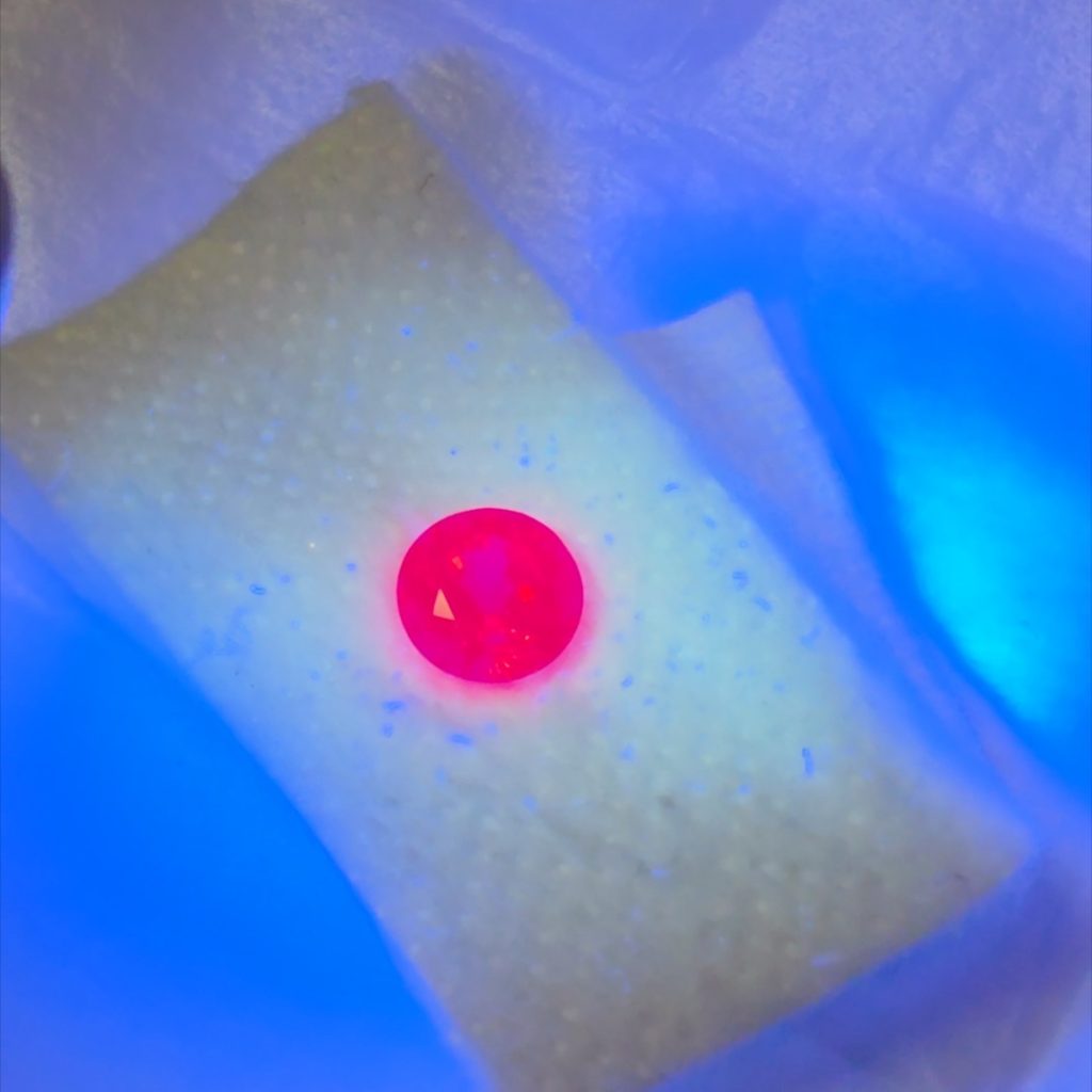 Jedi spinel glowing red under a UV torch on a white gem pad