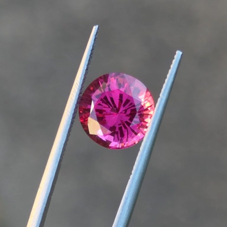 Neon Jedi spinel from Mogok held in gem tweezers, glowing magenta